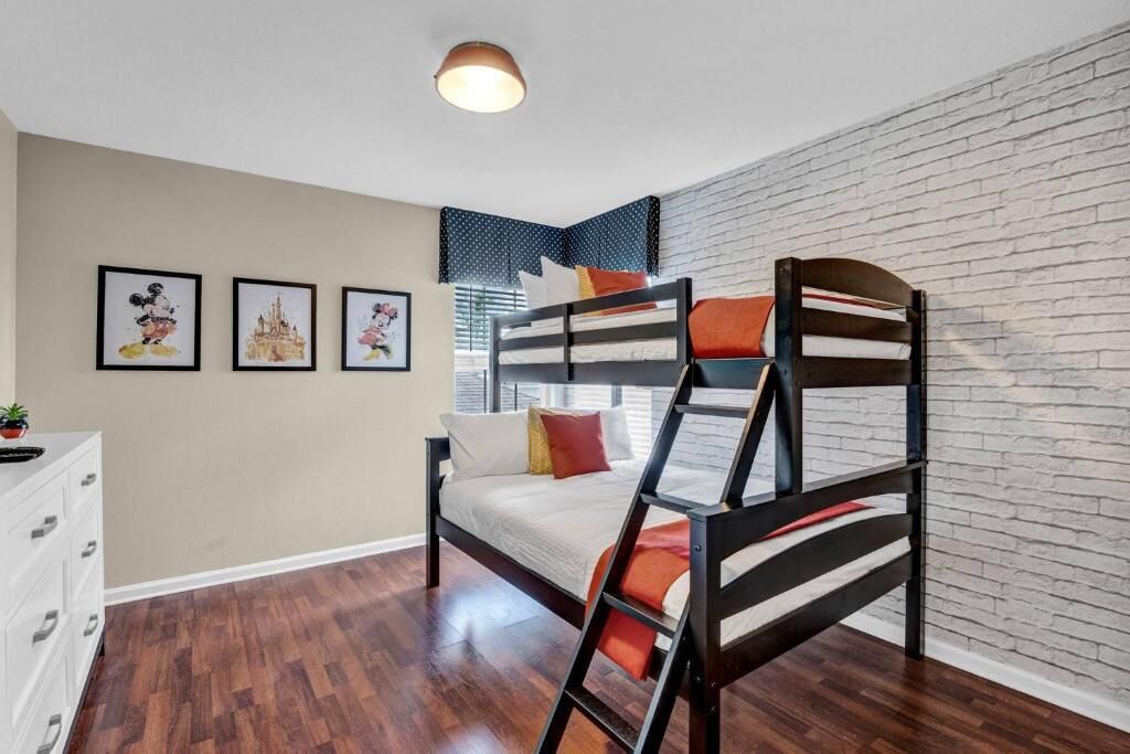 A bunk bed room with a white dresser, a brick wall, and three framed pictures on the wall.