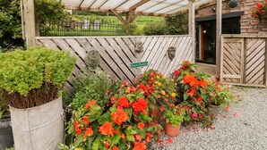 Een overdekt parkeergebied voor gasten, met een houten hek, een bord met daarop 'Gastenparkeren' en diverse potplanten met bloemen.