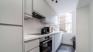 Una cocina moderna con armarios blancos, un horno negro y una ventana con rejas.