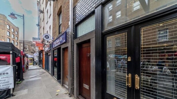 Una calle estrecha con comercios cerrados y una puerta negra con un ventanal.