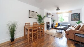 Una sala de estar moderna con una mesa de comedor de madera, un sofá y una mesa de centro. Hay una planta en maceta y un cuadro en la pared.