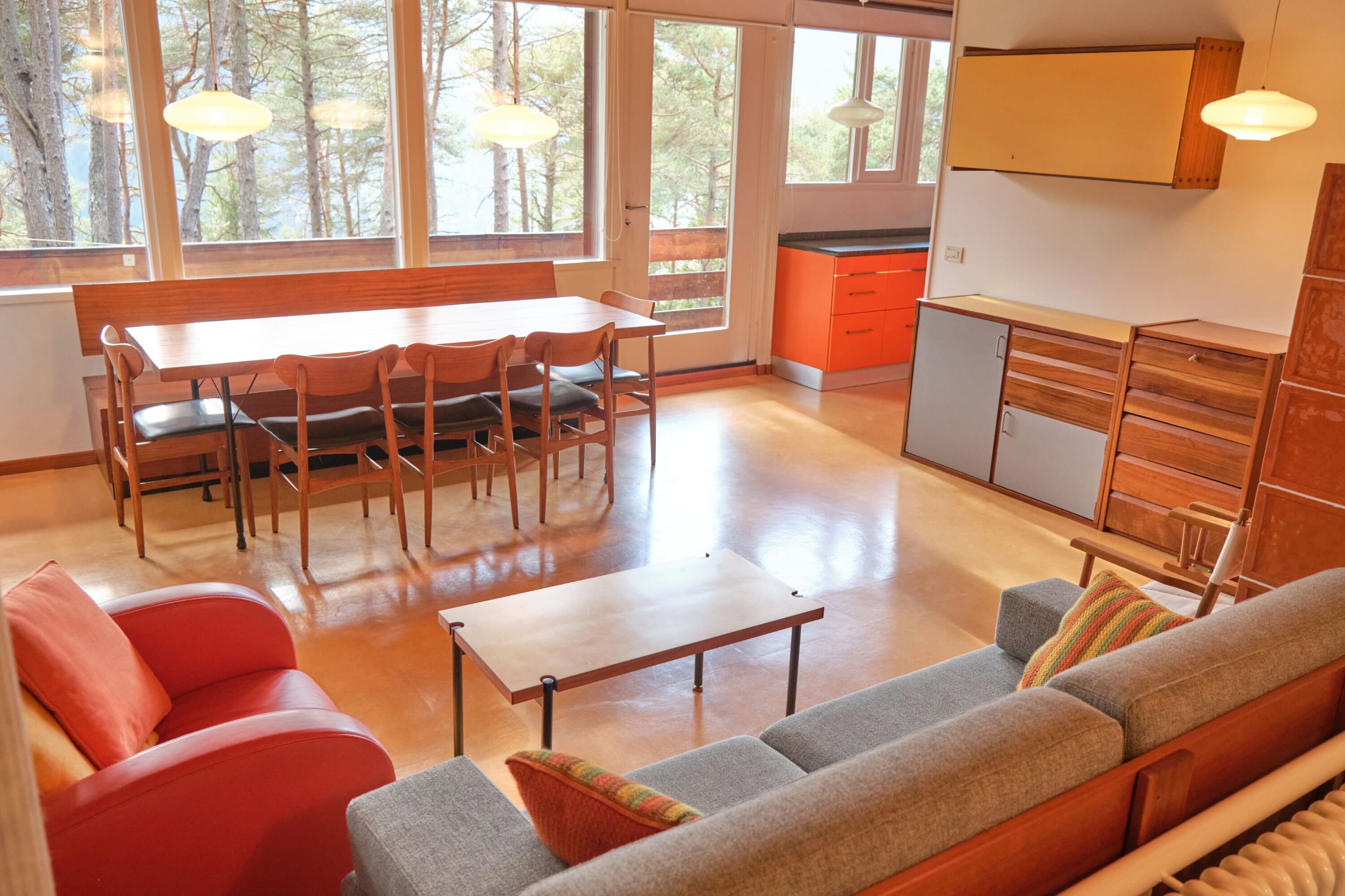 Ein geräumiger Wohnbereich mit einem Holzesstisch, roten und grauen Sofas und einer Küche mit orangefarbenen Schränken.