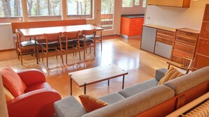 Amplia sala de estar con una mesa de comedor de madera, sofás rojos y grises, y una cocina con armarios color naranja.