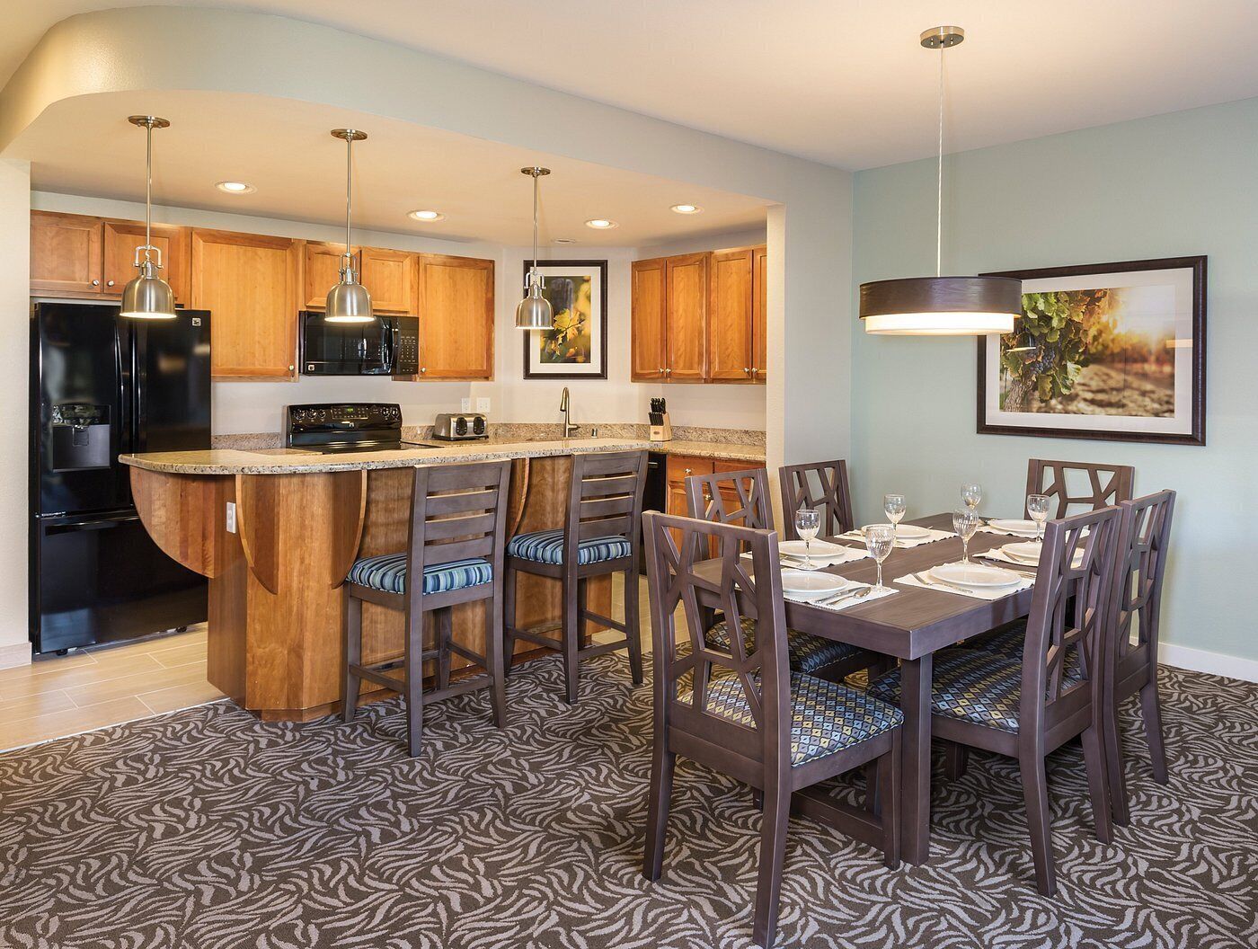 A modern kitchen with wooden cabinets, a black refrigerator, and a bar area with bar stools.