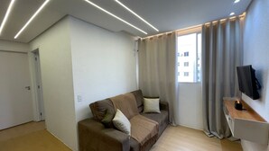 A modern living room with a brown sofa, a flat-screen TV mounted on the wall, and a wooden desk with a lamp.