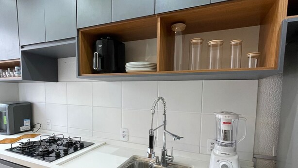 A modern kitchen with grey cabinets, a white countertop, a built-in stove, a sink with a faucet, and a blender.