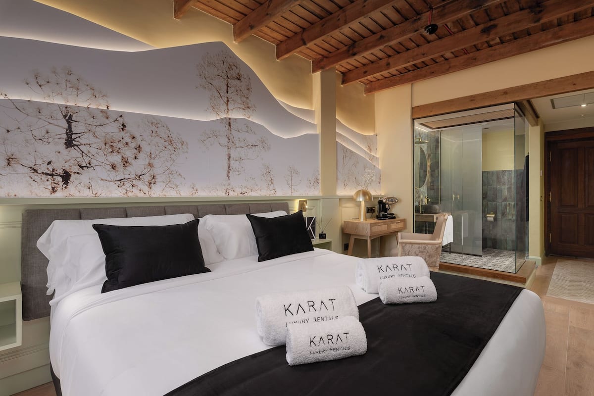 Habitación de hotel moderna con una cama grande, zona de ducha de vidrio y un mural original en la pared.