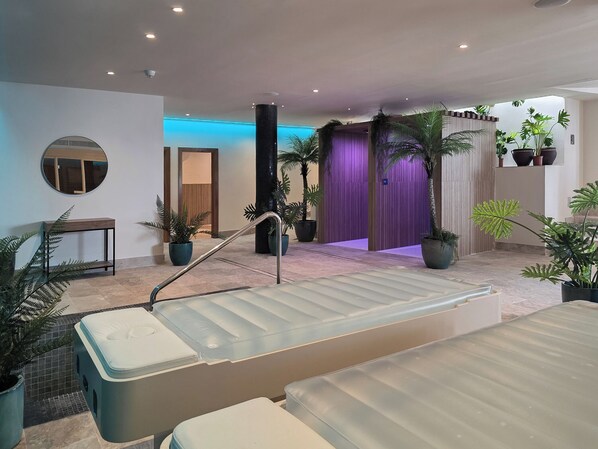 Zona de spa con camilla de masaje, plantas en macetas y una cortina morada.