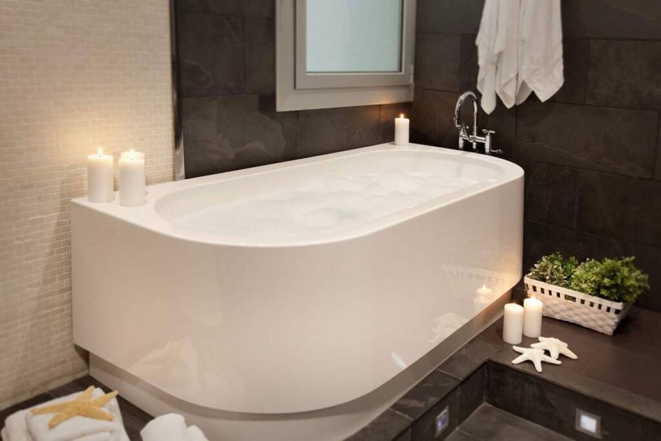 A modern bathroom with a freestanding bathtub, two lit candles, a small plant, and a starfish decoration.