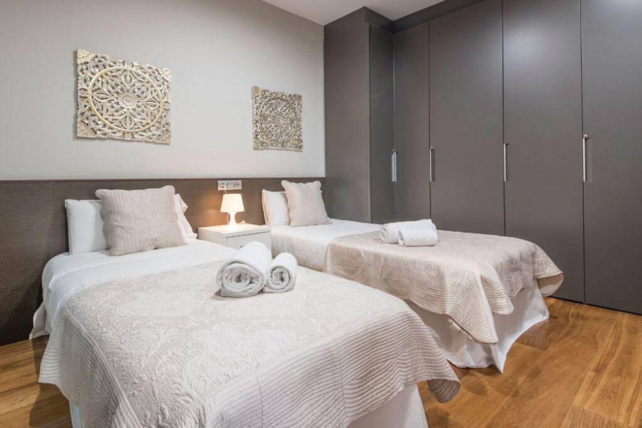 Et hotelværelse med to senge, et natbord, billedkunst på væggen og et klædeskab.