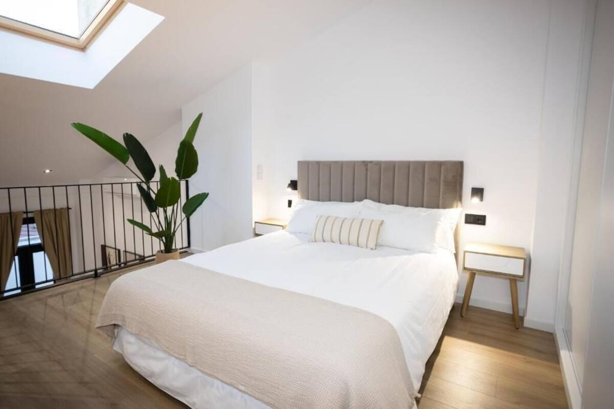 A modern bedroom with a large bed, a skylight, a potted plant, and a view of the balcony.
