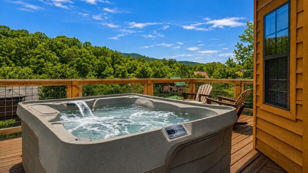 Un bain à remous sur une terrasse en bois, avec vue sur une colline boisée.
