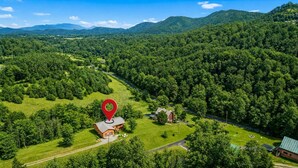 Un paysage rural avec une maison signalée par une épingle rouge sur une carte, entourée de forêts denses et de collines.