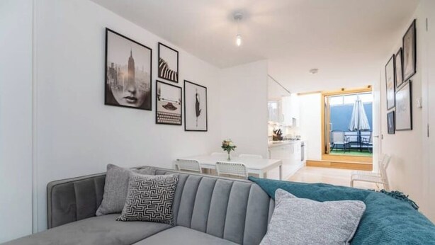 Una sala moderna con un sofá gris, una manta color turquesa y obras de arte enmarcadas en la pared.