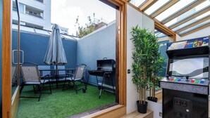 Un espacio habitable compacto con un pequeño patio que cuenta con una parrilla, mobiliario exterior y una planta en maceta.
