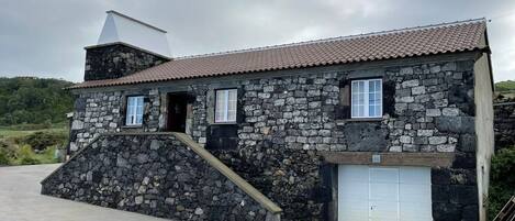 A stone building with a tiled roof, a ramp leading to the entrance, and a garage door.