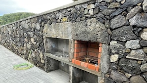 Een stenen muur met een ingebouwde barbecue en een tuinslang op de grond.