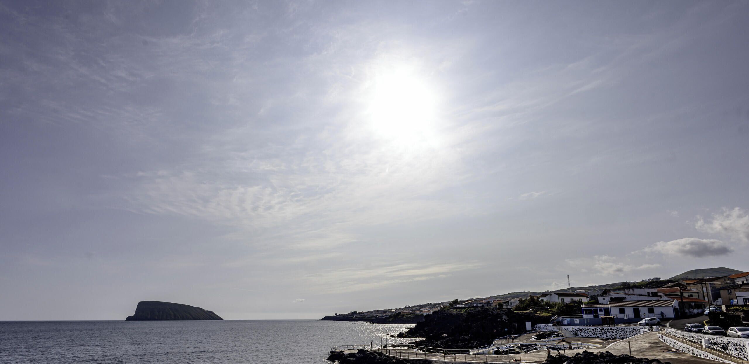 A coastal town with a prominent hill, a clear sky, and a sunlit sea.