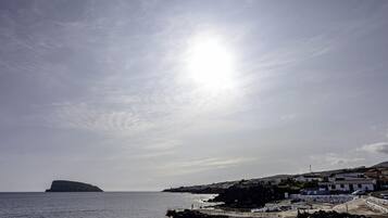 A coastal town with a prominent hill, a clear sky, and a sunlit sea.