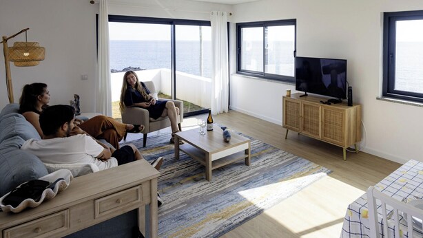 Un salon moderne avec un canapé, une table basse, un téléviseur et une vue sur la mer.