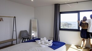 Une chambre d’hôtel moderne dotée d’un grand lit, d’un coin salon avec un fauteuil, d’un miroir et offrant une vue sur la mer.