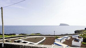 Une vue sur la côte, avec un sentier en pierre menant à un jardin circulaire, un lampadaire et une série de structures blanches et bleues.