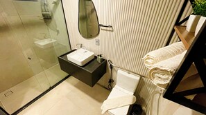 Un baño moderno con cabina de ducha de vidrio, tocador negro con lavamanos blanco y toallero con toallas dobladas.