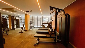 Un gimnasio con diverso equipo de ejercicio, una banca y una pared con un cartel.