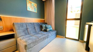 Ein modernes Wohnzimmer mit einem grauen Sofa, zwei gemusterten Kissen, einer Wandpaneele aus Holz, einem gerahmten Kunstwerk und einem großen Fenster mit Vorhängen.