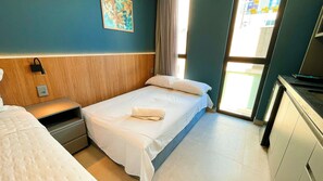 Ein Hotelzimmer mit zwei Betten, einem Holzkopfstück, einem Bild an der Wand und Blick auf die Straße durch das Fenster.