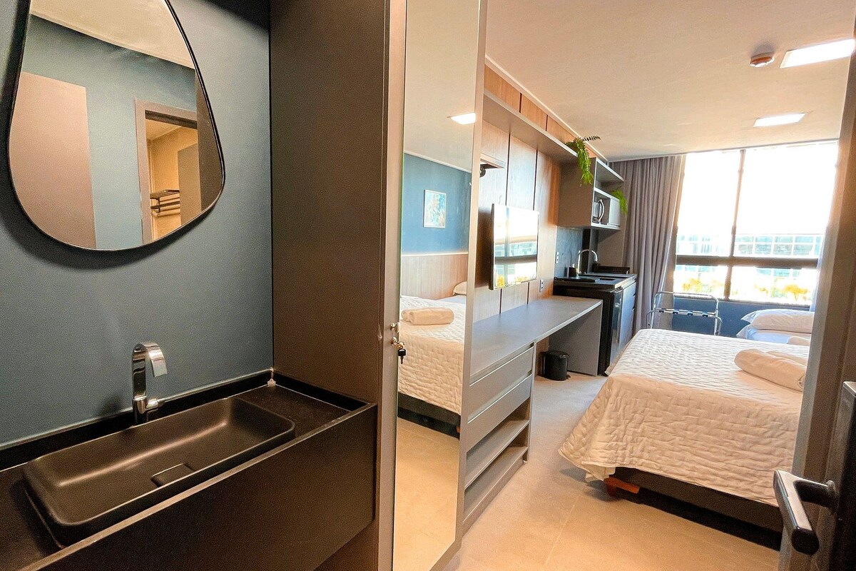 Una habitación de hotel moderna con un espejo grande, un lavabo, una cama, un escritorio y una ventana con vistas.