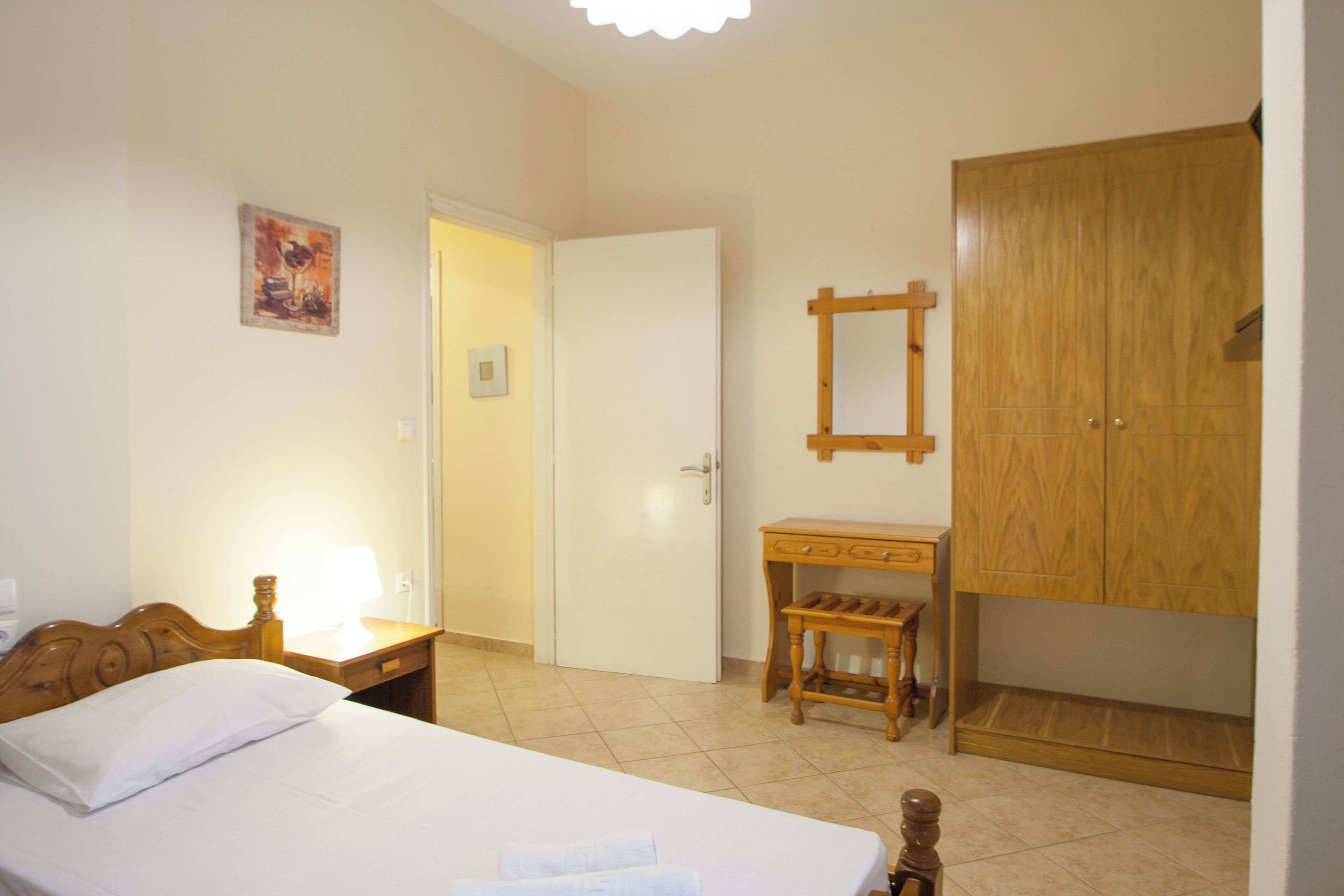 Un dormitorio con cama, mesita de noche, armario de madera y un pequeño banco de madera.