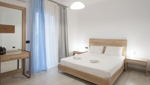 Une chambre d’hôtel moderne avec un lit en bois, une table de chevet, une commode, un miroir et une fenêtre ornée de rideaux légers.