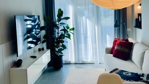 A modern living room with a sofa, a dining table, a TV, and a large plant. - Blueyes House Tuscany (Montespertoli)