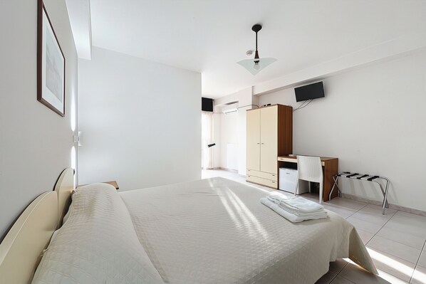 Une chambre à coucher avec un lit, un bureau, une chaise, une armoire et un téléviseur fixé au mur.