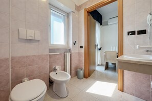 Un baño con inodoro, bidé y lavamanos, una ventana y vista a otra habitación.