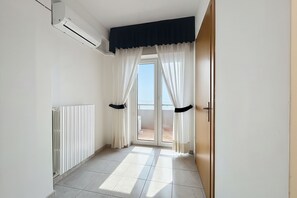A hallway with a radiator, a sliding glass door leading to a balcony, and a door with a black handle. - B&B Sea View with Balcony - 104 - Santangelo - Pool (Monte Sant'Angelo)