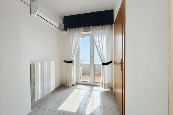 Un corridoio con un termosifone, una porta scorrevole in vetro che dà su un balcone e una porta con maniglia nera.