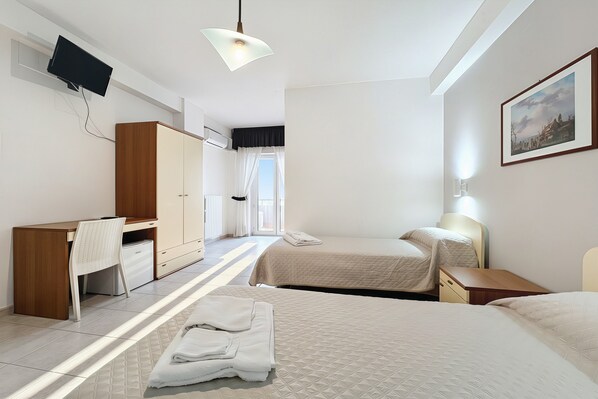 A hotel room with two beds, a desk, a chair, a wardrobe, a television mounted on the wall, and a window with curtains. - B&B Sea View with Balcony - 104 - Santangelo - Pool (Monte Sant'Angelo)