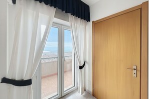 A room with a sliding glass door leading to a balcony, a wooden door, and sheer curtains. - B&B Sea View with Balcony - 104 - Santangelo - Pool (Monte Sant'Angelo)