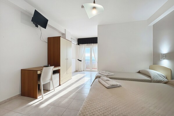 Habitación de hotel con escritorio, silla, dos camas, televisor y vistas al exterior.