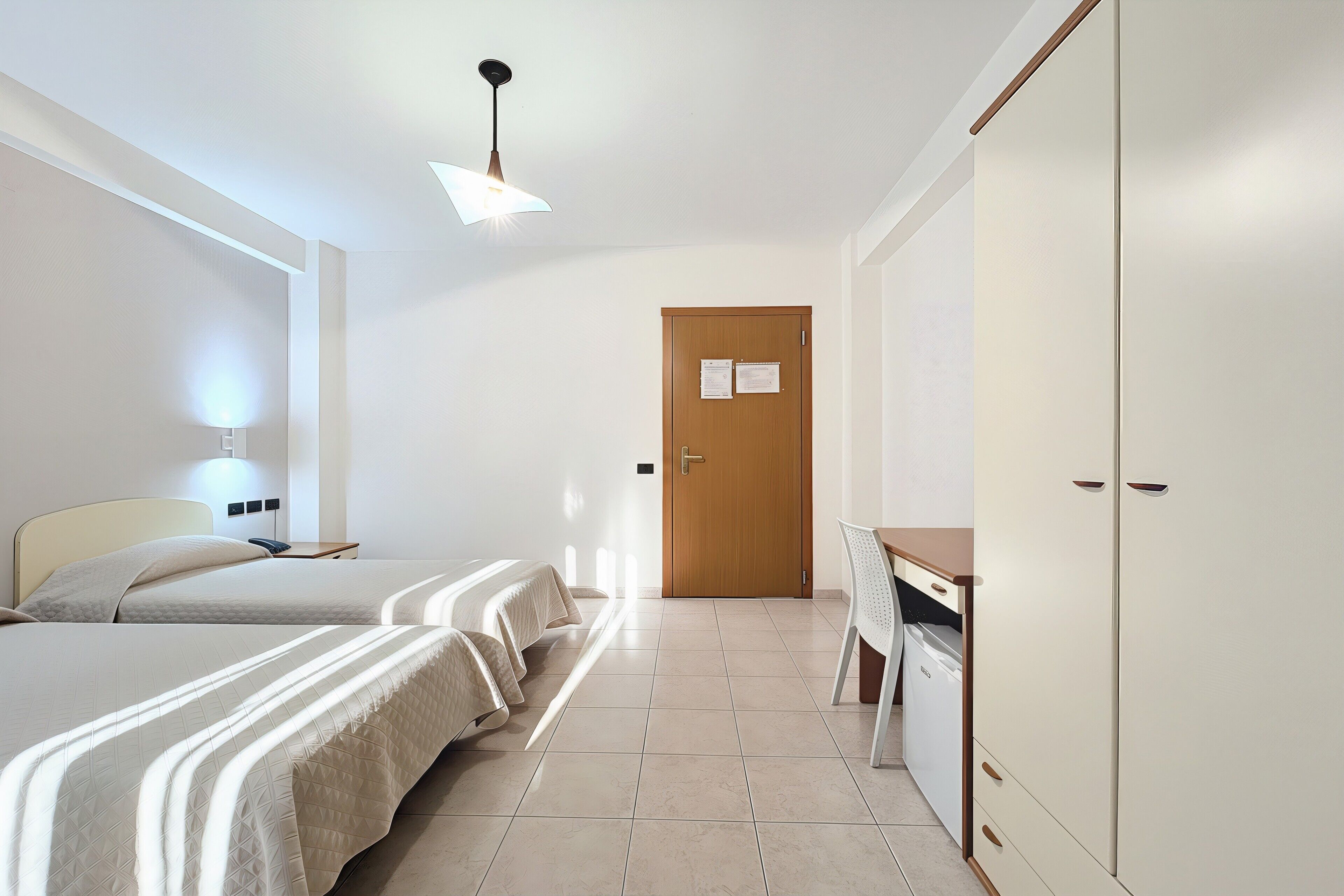 Ein Hotelzimmer mit zwei Betten, einem Schreibtisch, einem Kleiderschrank und einer Tür mit einem Zettel.