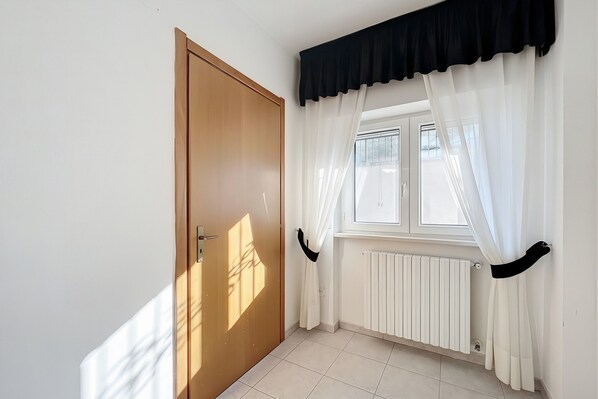 A room with a wooden door, a window with white curtains, and a radiator. - B&B with Window - 107 - Santangelo - Pool (Monte Sant'Angelo)