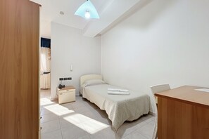 Ein Schlafzimmer mit Bett, Nachttisch, Stuhl, Schreibtisch und einem kleinen Fenster.