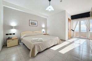 Una camera d'albergo con un letto, comodini, una lampada a parete, un quadro incorniciato e vista dalla finestra.