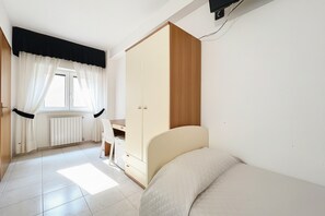 Un dormitorio con cama, escritorio, armario y ventana con cortinas.
