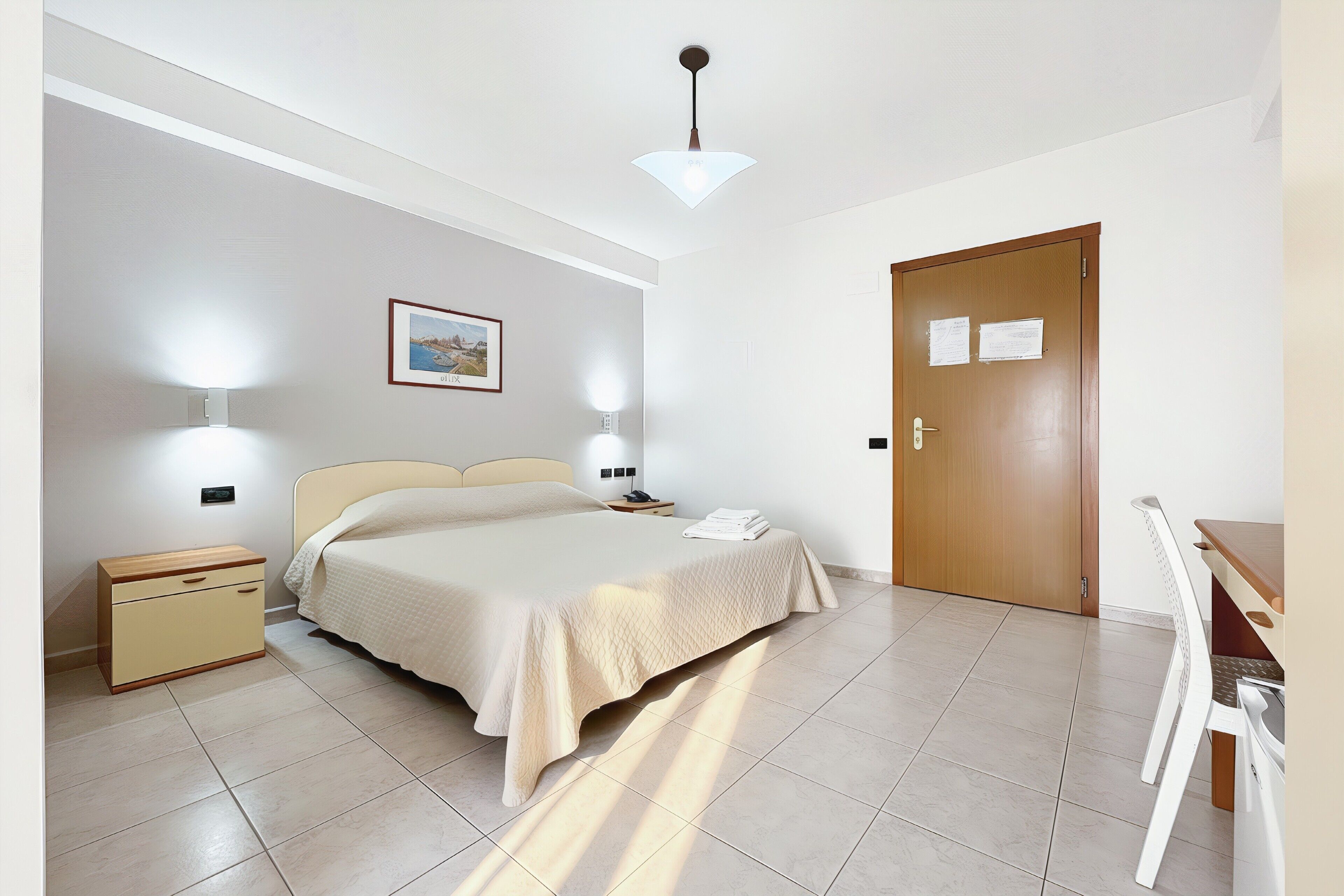 Un dormitorio con cama, mesitas de noche, una puerta de madera y un escritorio con sillas.