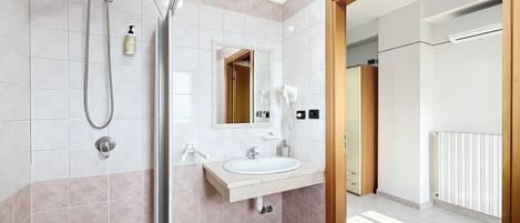A modern bathroom with a shower, sink, mirror, and a view of the hallway.