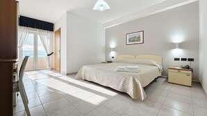Un dormitorio con cama, mesitas de noche, escritorio, silla, ventana con cortinas, una lámpara en el techo e imagen colgada en la pared.