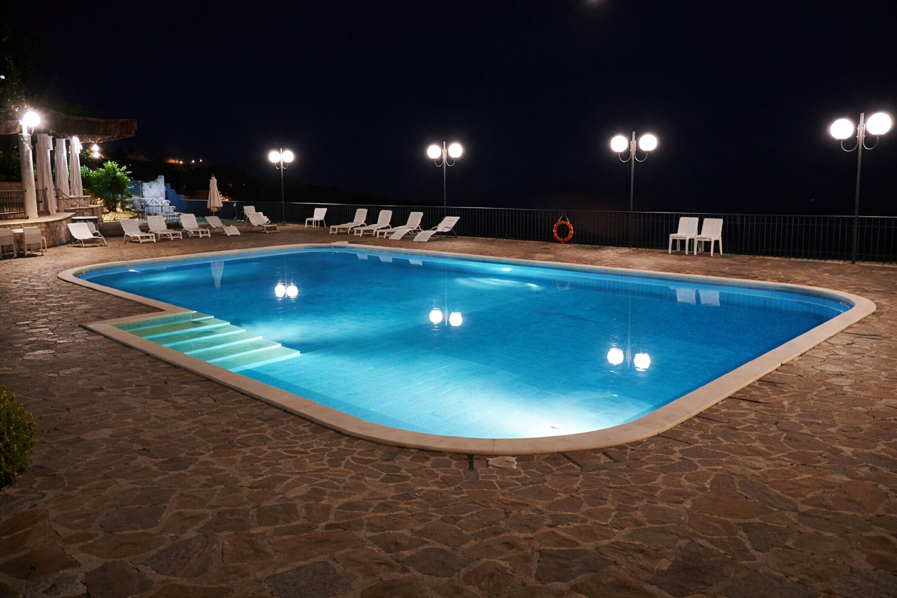 A swimming pool with lounge chairs and lights at night.
